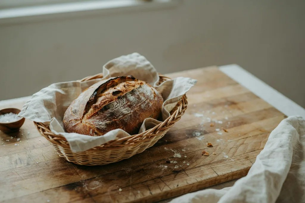 A rustic oval hearth loaf with a blistered amber crust and a dramatic curved ear, resting in a linen-lined basket.
