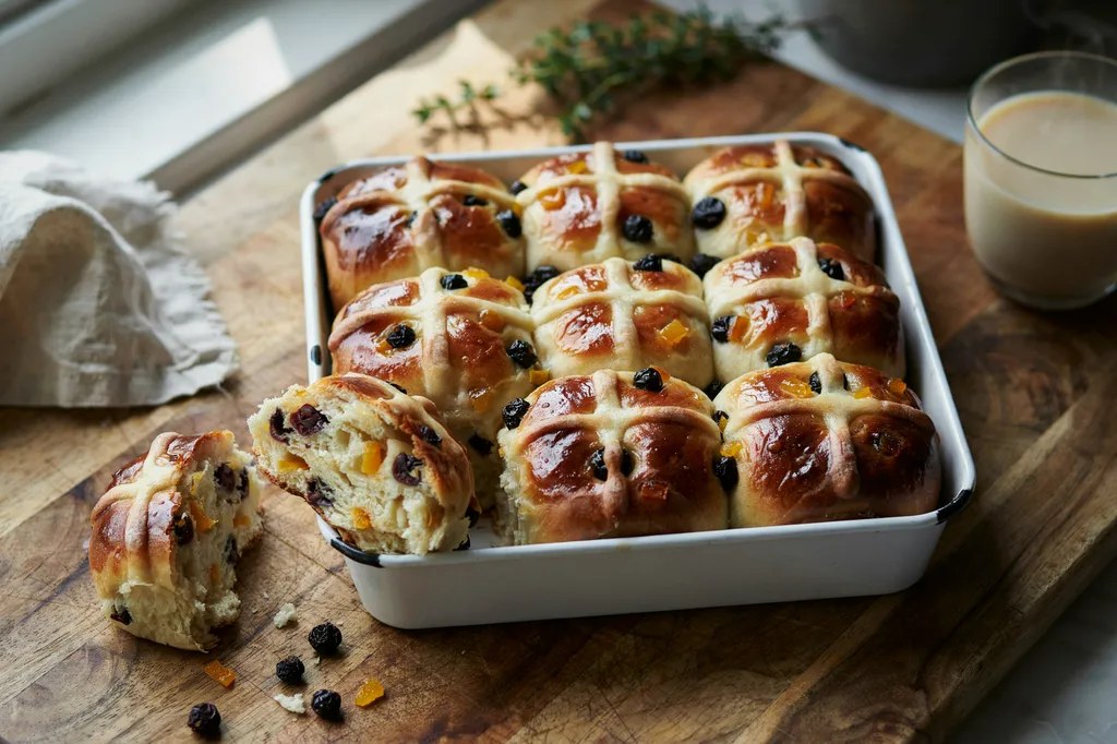 Hot cross buns in a square tin, glossy-glazed with piped white crosses, studded with currants and candied peel.