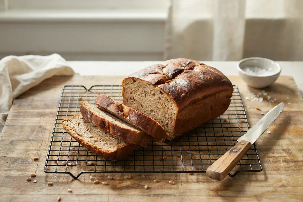 A 100% whole wheat sandwich loaf on a cooling rack, half sliced into even slices showing a soft brown crumb.