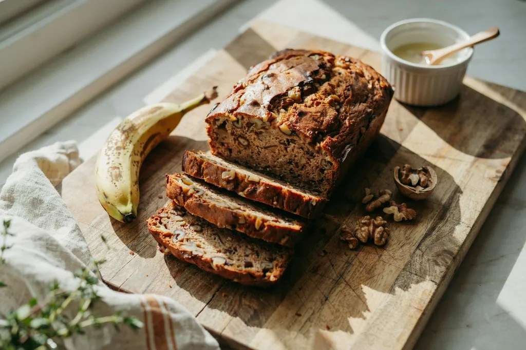 A whole grain banana bread loaf with a cracked top, thick slices showing a moist dark speckled crumb.