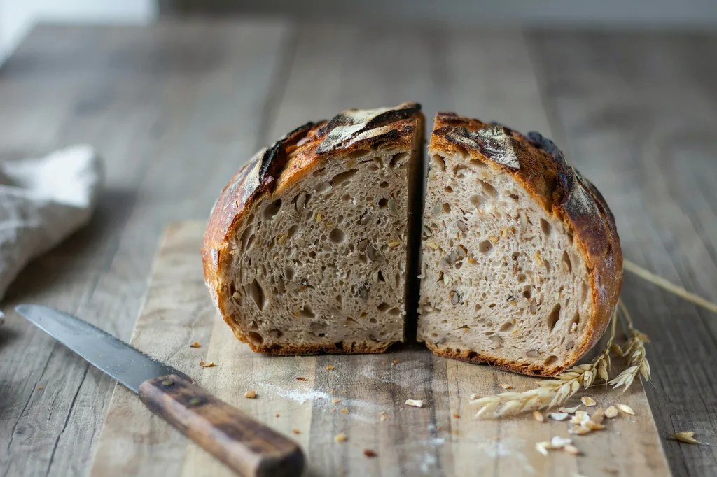 A round 100% whole wheat sourdough loaf cut in half, both halves stood upright showing a brown crumb dense with bran flecks.