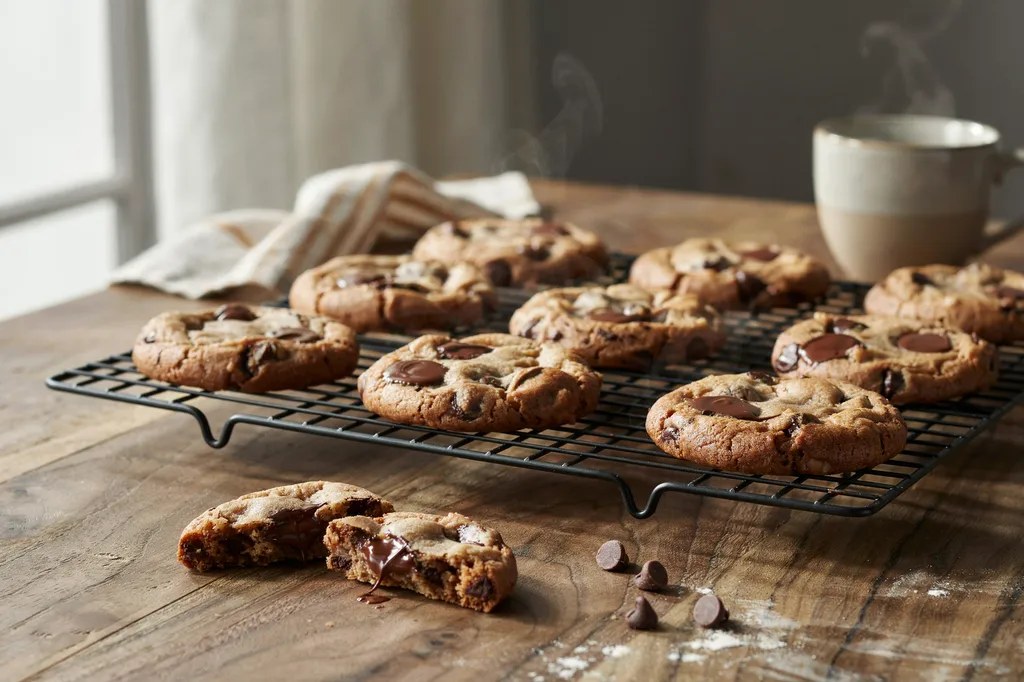 Chewy einkorn chocolate chip cookies cooling on a wire rack, one broken in half showing molten chocolate.