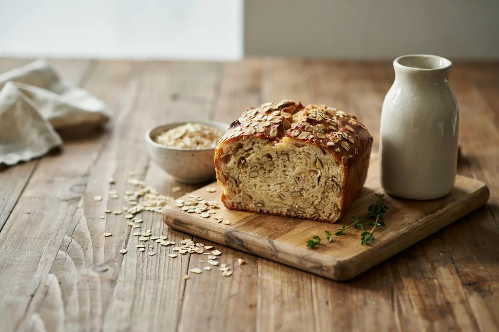 A soft oatmeal sandwich loaf scattered with rolled oats across the top, sliced to show a moist crumb speckled with oats.
