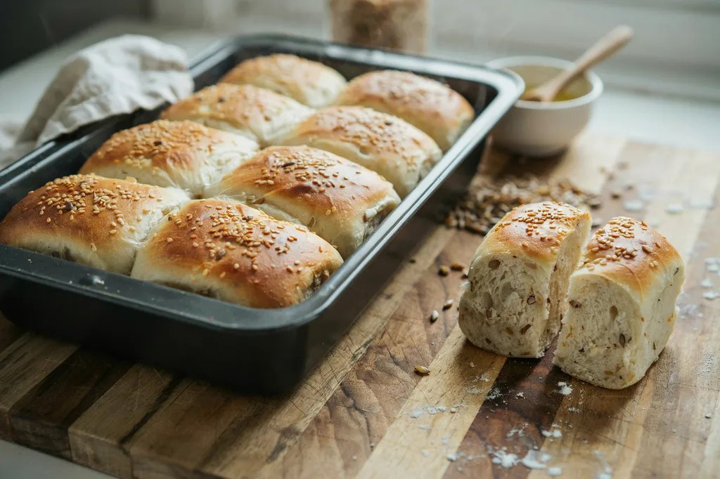 Soft whole grain hot dog buns joined in a row in a pan, one pulled away and split showing a soft interior.