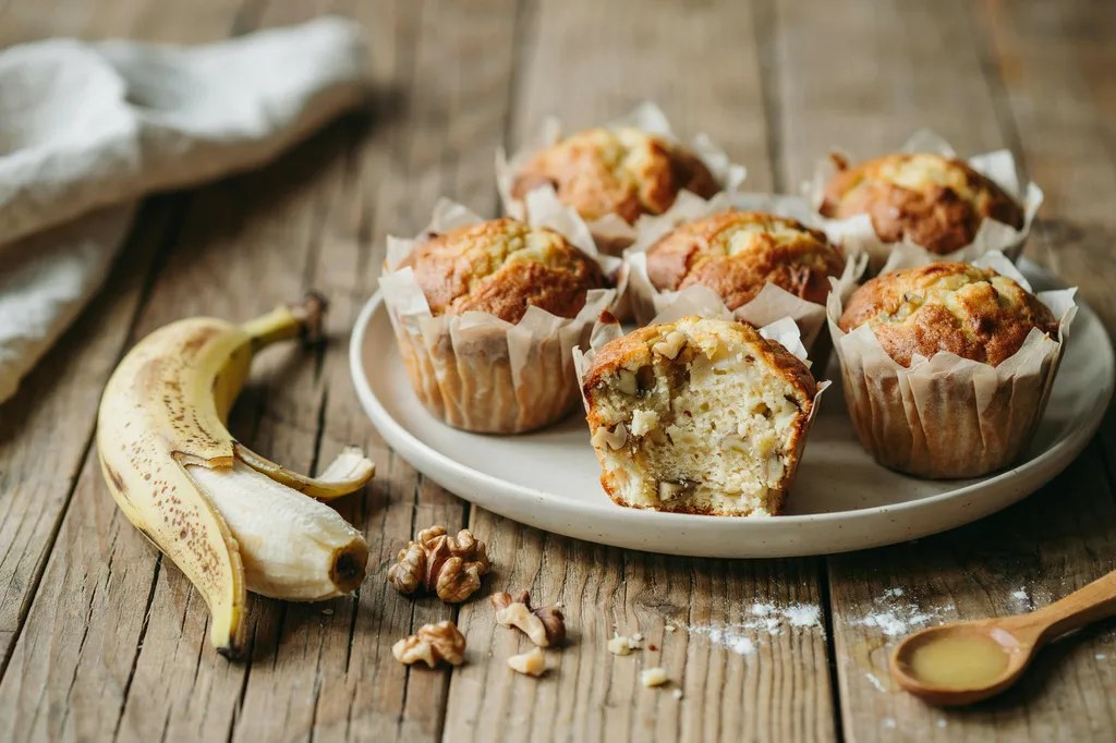 Einkorn banana muffins with domed golden tops, one split open showing a very moist tender pale-gold crumb.