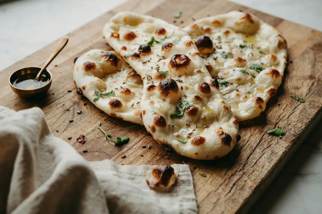 Three teardrop-shaped whole grain naan breads, puffed and charred, glossy with butter and scattered with coriander.