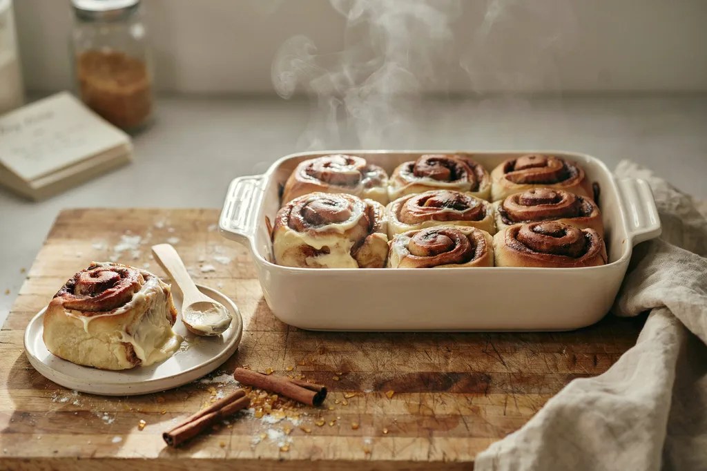 Whole grain cinnamon rolls with cream cheese frosting melting over the warm spirals, one lifted out showing soft layers.