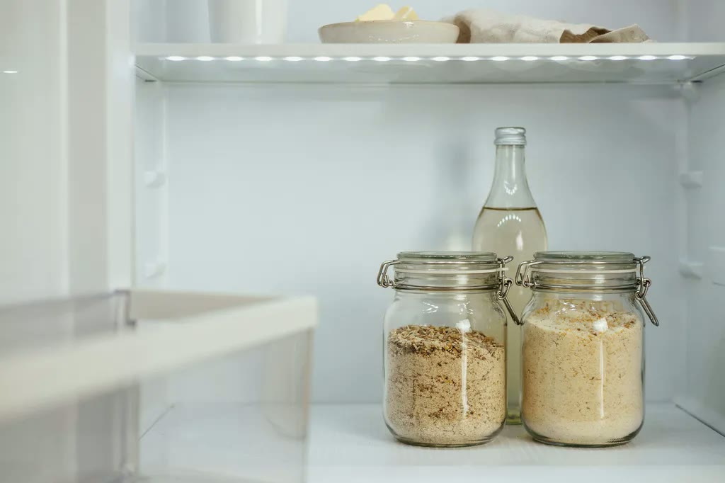Two airtight clamp-lid glass jars of fresh milled flour on a refrigerator shelf.