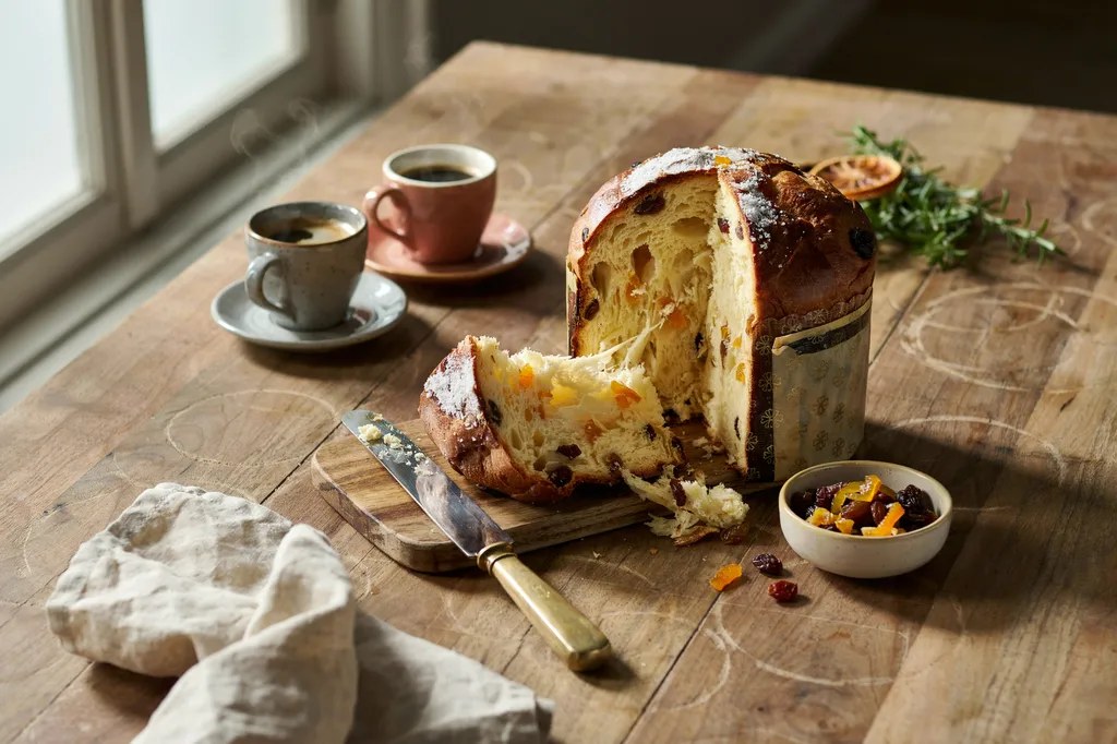 A tall domed panettone with a wedge cut away revealing an airy, shreddy vertical crumb studded with candied orange and raisins.