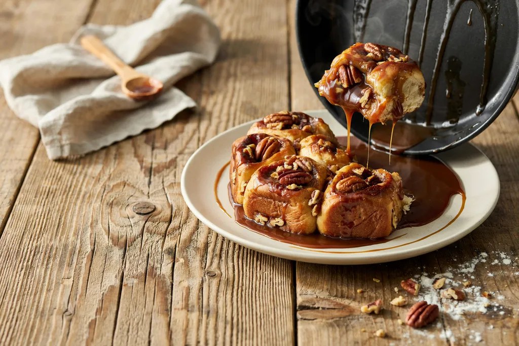 Sticky buns just inverted onto a plate, dark caramel running down the sides, studded with toasted pecans.