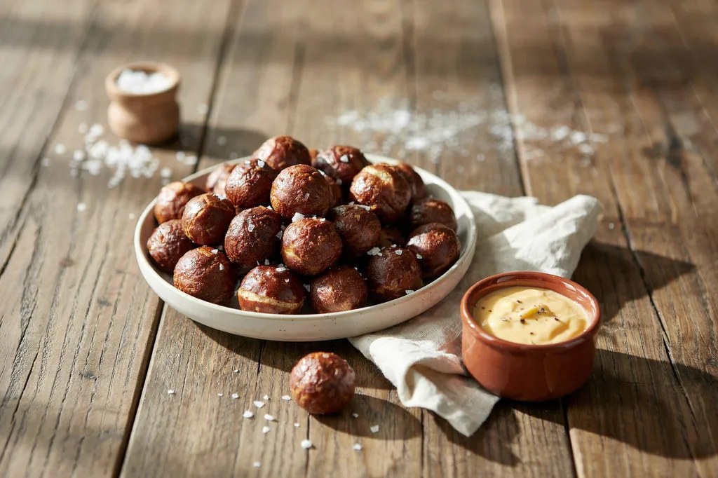 A bowl piled with small bite-sized pretzel nuggets, deep glossy brown and scattered with coarse salt.