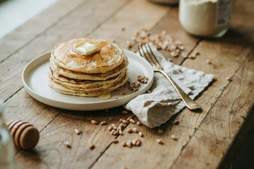 A stack of pale golden einkorn pancakes, more delicate than whole wheat, with butter melting and honey drizzled over.