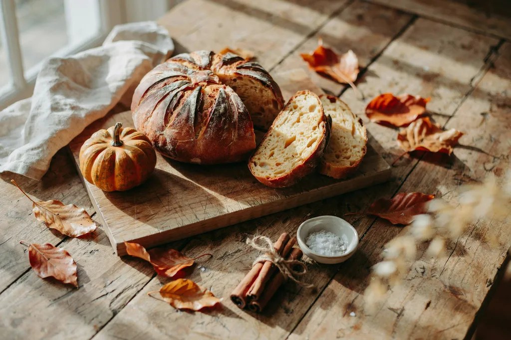 A round pumpkin sourdough loaf scored in a radiating wedge pattern, slices showing a warm orange-tinted crumb.