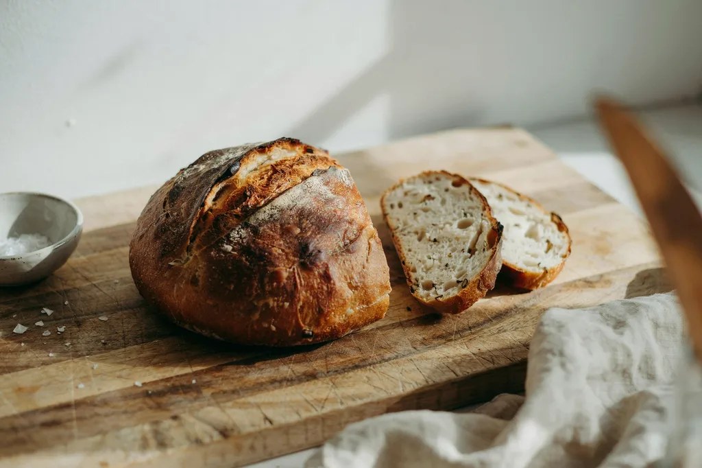 A round whole grain sourdough boule with a bloomed score and two thick slices cut, showing an open bran-flecked crumb.